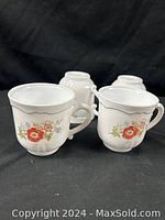 Four vintage Arcopal France milk glass teacups with orange and white poppy and blue Forget-Me-Not floral design displayed on black background, viewed from front and back sides.