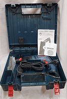 Bosch 11258VSR hammer rotary drill inside the molded hard plastic carrying case along with instruction manuals and drill bits visible on the left side compartment.
