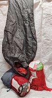 Grey North Face sleeping bag with red lining and hood, packed with two other sleeping bags.
