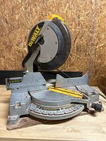 Front view of the DeWalt miter saw placed on a wooden surface showing the blade guard, metal base with angle adjustments, and fence.