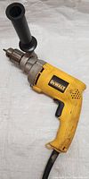 Full view of DeWalt drill showing rubber grip handle, metal chuck, attached 360-degree side handle, and power cord.