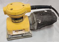 Front side view of the yellow DeWalt DW411 palm grip hand sander showing the dust collection bag attached at the rear with visible signs of use, paint marks, and dust residue on sander base and body.