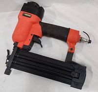 Full side view of the Husky brad nailer showing orange and black casing, magazine, trigger, and hose connector.