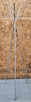 Full height image of the Ikea metal coat rack standing against a wood panel background, showing tripod legs and upper hooks.
