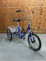 Full view of blue foldable tricycle showing front wheel, frame, saddle and rear basket