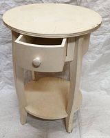 Full view of the white round side table with drawer partially open, showing wear and dirt.