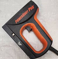 Full view of PowerShot Pro electric stapler and nailer showing black and orange body with trigger and cord.