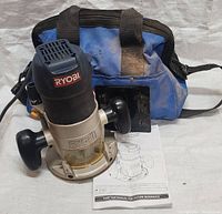 Ryobi R163 fixed base router with blue and black tool bag and instruction manual, viewed from above showing front of the router and handles, with some visible wear and dirt on the bag.