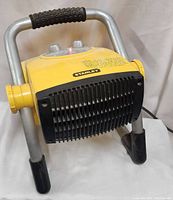 Front view of yellow Stanley ceramic heater showing front black grille and tubular metal frame stand with rubber feet and handle grip.