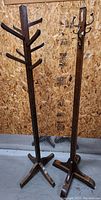 Two vintage wooden coat racks side by side against a plywood wall, showing overall form and peg/hook layouts.
