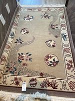 Full view of the rectangular beige area rug with circular floral motifs and symbolic border patterns, showing overall design and dimensions.