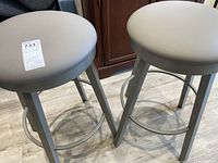 Pair of matching round grey vinyl cushioned swivel barstools with painted metal bases and footrests viewed from top down angle