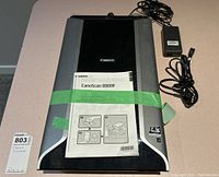 Canon CanoScan 8800F scanner with manual and power adapter/cords on a table.