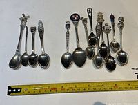 Full view of all 15 collector spoons arranged in a row with a measuring tape showing lengths of around 12-13cm approximately.