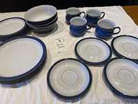 Overview of set with stacked dinner plates, bowls, saucers, mugs displayed on table.