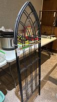 Photo showing one of the black metal garden trellises with gothic-arch top and grid lower section.
