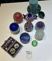 Top view of all items showing nine unique glass paperweights, a large teal candle on a mosaic base, and a small green decorative glass piece.