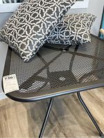 Two black and white geometric pattern outdoor cushions placed on the metal mesh patio table.