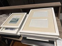 Stack of white picture frames including double photo windows with beige mats, showing size and condition.