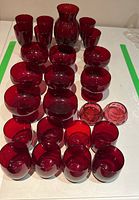 Full set of red glassware arranged on a table showing the variety of glasses, a pitcher, and decorative bowls.