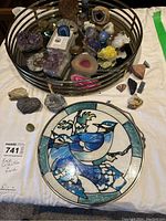 Full view of the rock collection in a metal tray with a decorative stained glass style plate with blue bird design beside it, also showing smaller specimens outside the tray on the white cloth.