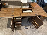 Wood veneer sewing cabinet with hinged top open revealing sewing machine and storage drawers.