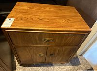 Full view of wooden side table showing top flat surface, single drawer with brass pull and two cabinet doors below with brass hardware.