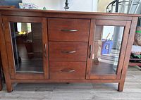Front view of wooden sideboard cabinet showing central drawers and glass doors