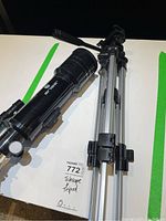 Photo showing black Brinno telescope alongside silver aluminum tripod on a white surface.