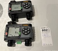 Two Melnor electronic watering timers placed on white surface to show front displays and controls with MaxSold lot tag