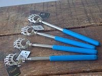 Four new metal back scratchers with bear paw-shaped scratching heads and blue rubberized handles, laid on wood surface