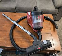 Bissell Zing II bagless canister vacuum with hose, adjustable wand, and floor nozzle, placed on wooden surface.
