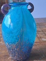 Side view of the thick blue glass vase with gold accents on the base and a rounded handle attached near the neck.