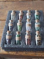 Full set of twelve labeled glass bottles filled with various polished stones arranged in a black foam holder.