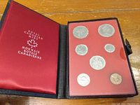 Photo showing the inside of a black leather presentation case with a red insert containing seven Canadian coins.