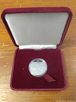 Photo showing the silver commemorative dollar coin in a maroon velour box with white liner.