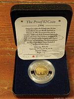 Bi-metallic $2 proof coin displayed in original black velvet-lined case with informational card including specifications and design details.