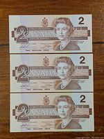 Front view of three 1986 Canadian two dollar bills showing Queen Elizabeth II portrait and denomination '2'.