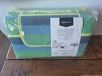 View of the picnic blanket folded with Amazon Basics label visible on packaging, showing colorful stripes and size details.