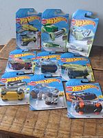 Nine unopened Hot Wheels toy vehicle packages arranged on wood surface, showing a variety of colors and models including helicopter and cars.