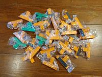 Photo of all 30 magnetic clips in orange and green, individually wrapped in plastic, laid out on a wooden surface.