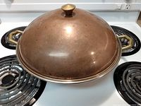 Top view showing the domed lid with a central knob on the wok, highlighting the round copper plated surface.