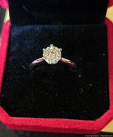 Front view of sterling silver ring with round Moissanite stone set in six-prong setting on polished band, displayed in black velvet-lined red box.