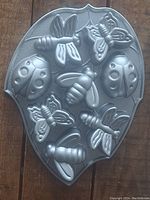 Top down view of first aluminum muffin tin shaped with insects including ladybugs, bees, and butterflies.