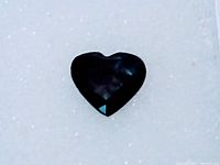 Heart-shaped deep blue sapphire gemstone photographed on white background, showing color and facets.