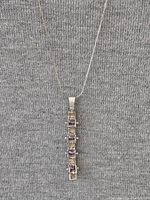 Vertical pendant necklace with alternating square purple zirconium and black stones on a fine sterling silver snake chain against gray fabric background.