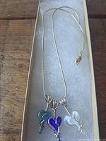 Sterling silver necklace with three colored glass heart pendants on a white padded background.