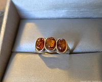 Photo of sterling silver ring featuring three oval amber stones arranged horizontally in a neutral fabric-lined box.