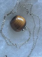 Apple-shaped tiger's eye pendant attached to sterling silver chain on a grey background.