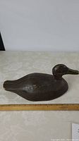 Side view of wooden black duck decoy showing full length and shape with ruler for scale.